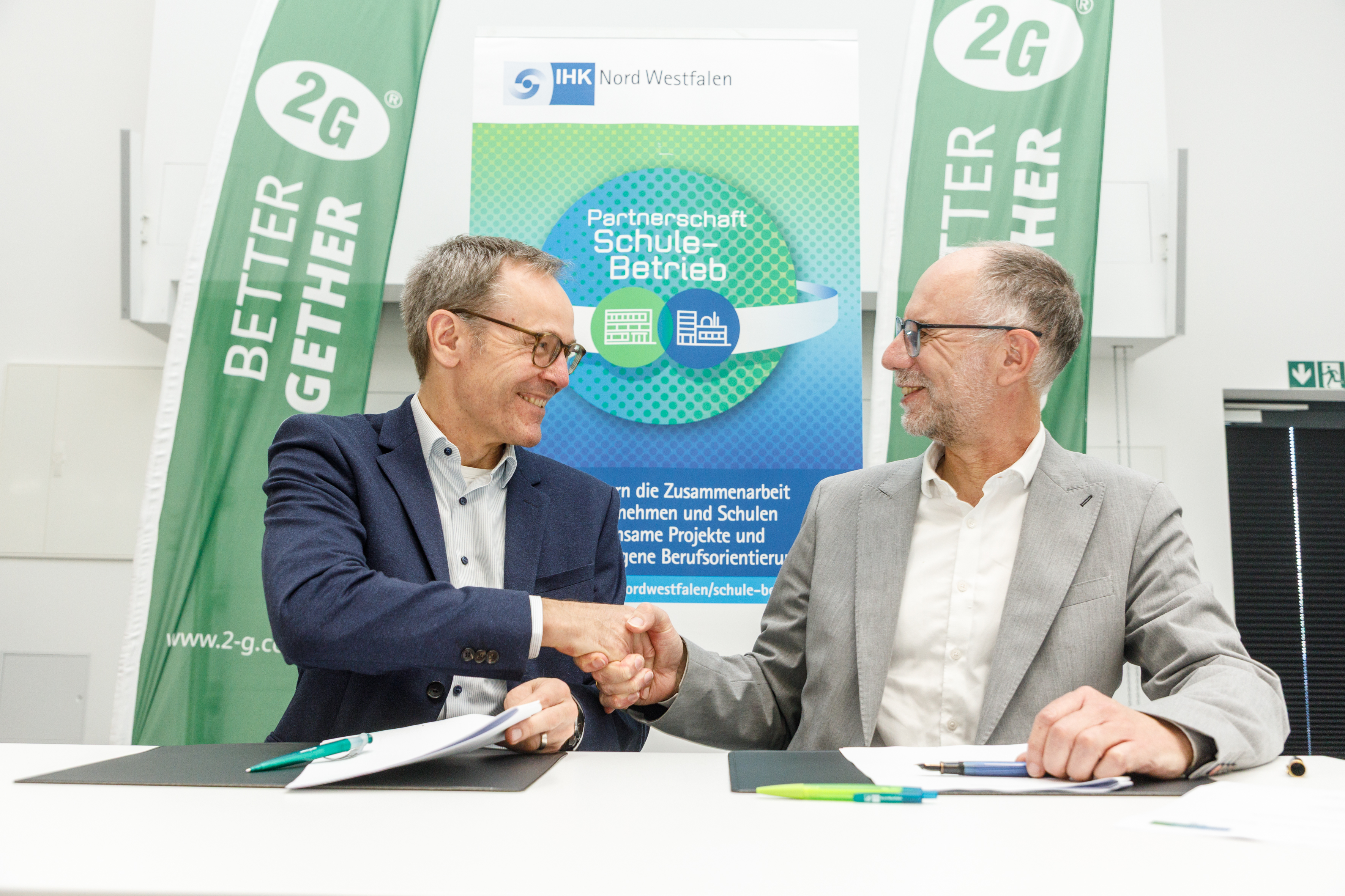 Michael Hinz und Klaus Schneider geben sich am Tisch mit den Vereinbarungen die Hand.